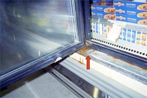 An open glass door in the freezer section of a grocery store with an arrow pointing to rust.