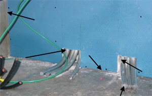 A blue wall with two sections at the base where gray tubes pass through. Black arrows point to various locations where there is an air leakage.